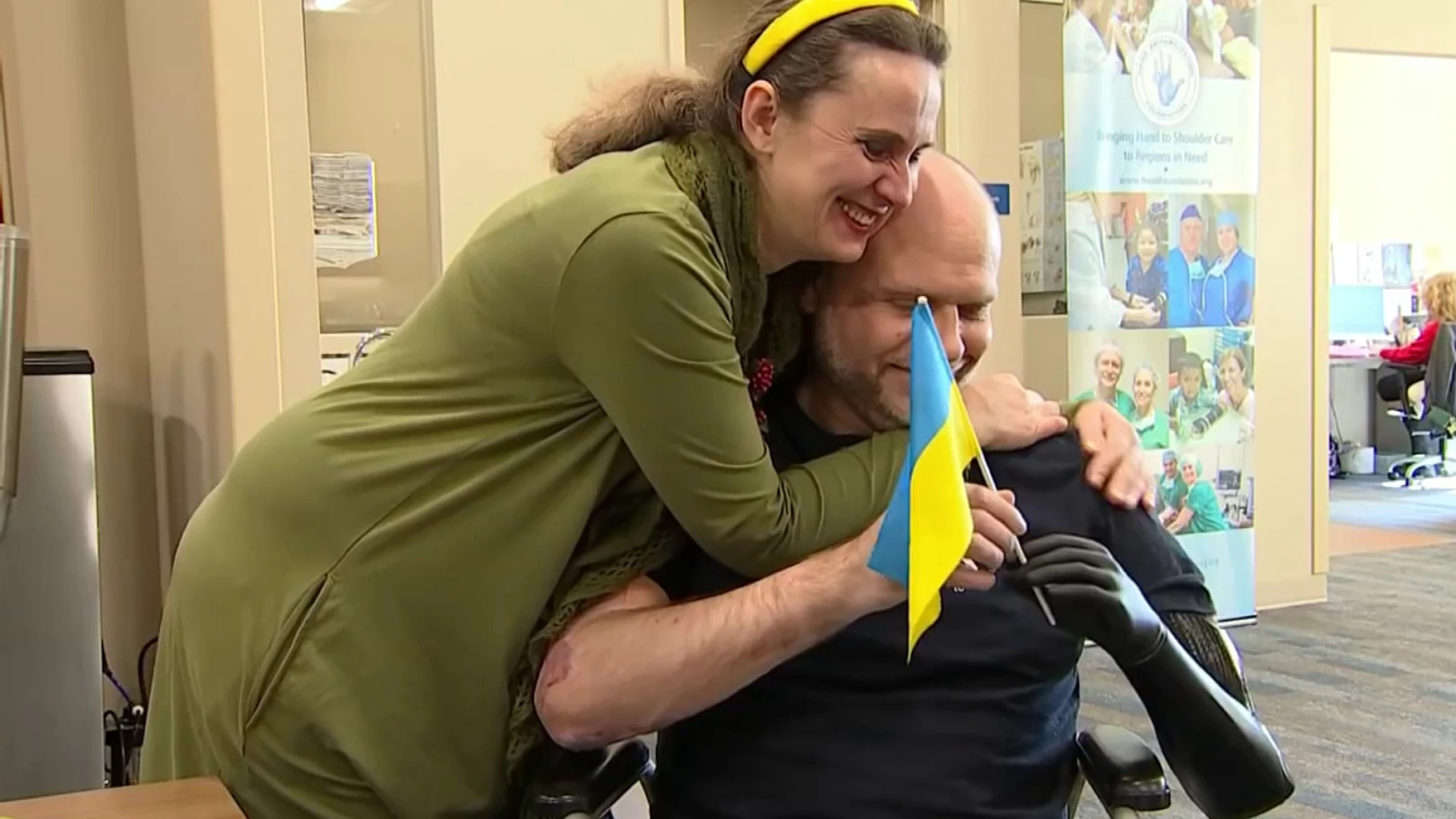 A person hugging an injured patient holding a Ukrainian flag.