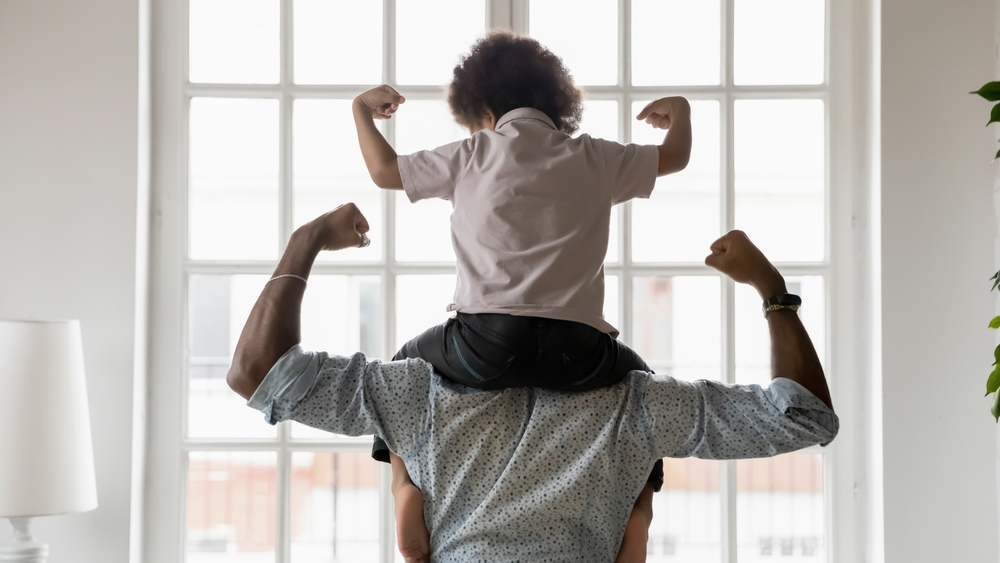 Young son sitting on his father's shoulders as they flex their muscles