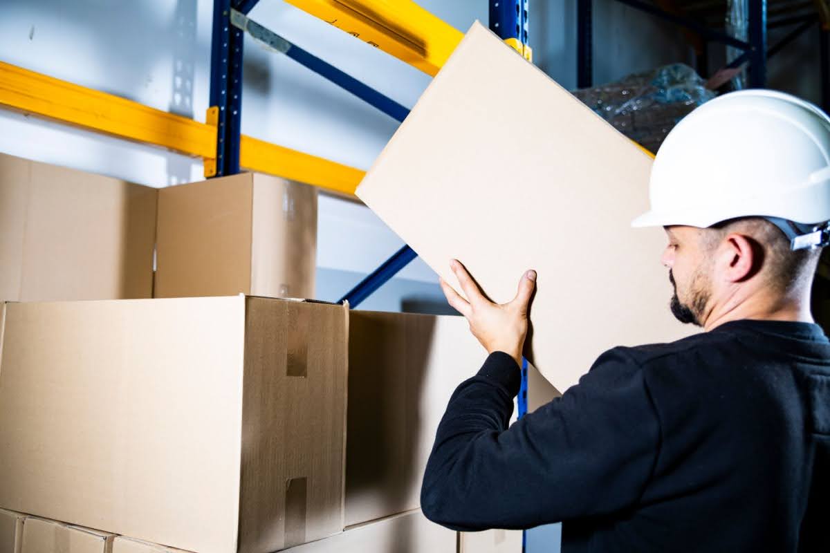 warehouse worker lifting a box onto a stack of other boxes using proper lifting techniques