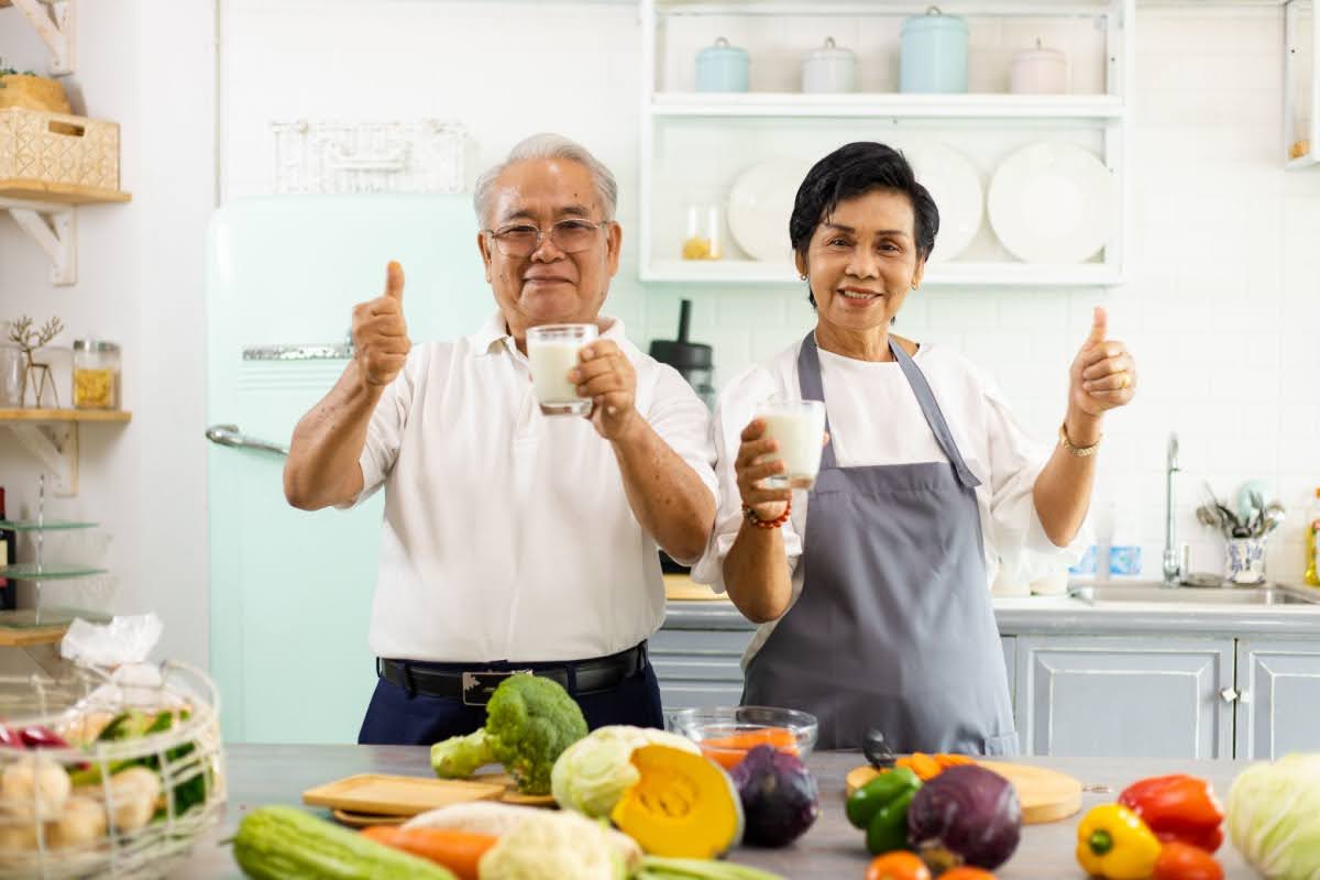 An older couple standing in their kitchen, surrounded by healthy food for strong bones and joints